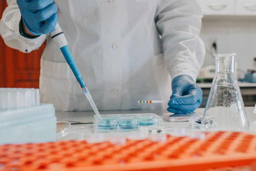 Stół laboratoryjny. Osoba pipetuje. Widoczne probówki, kolby