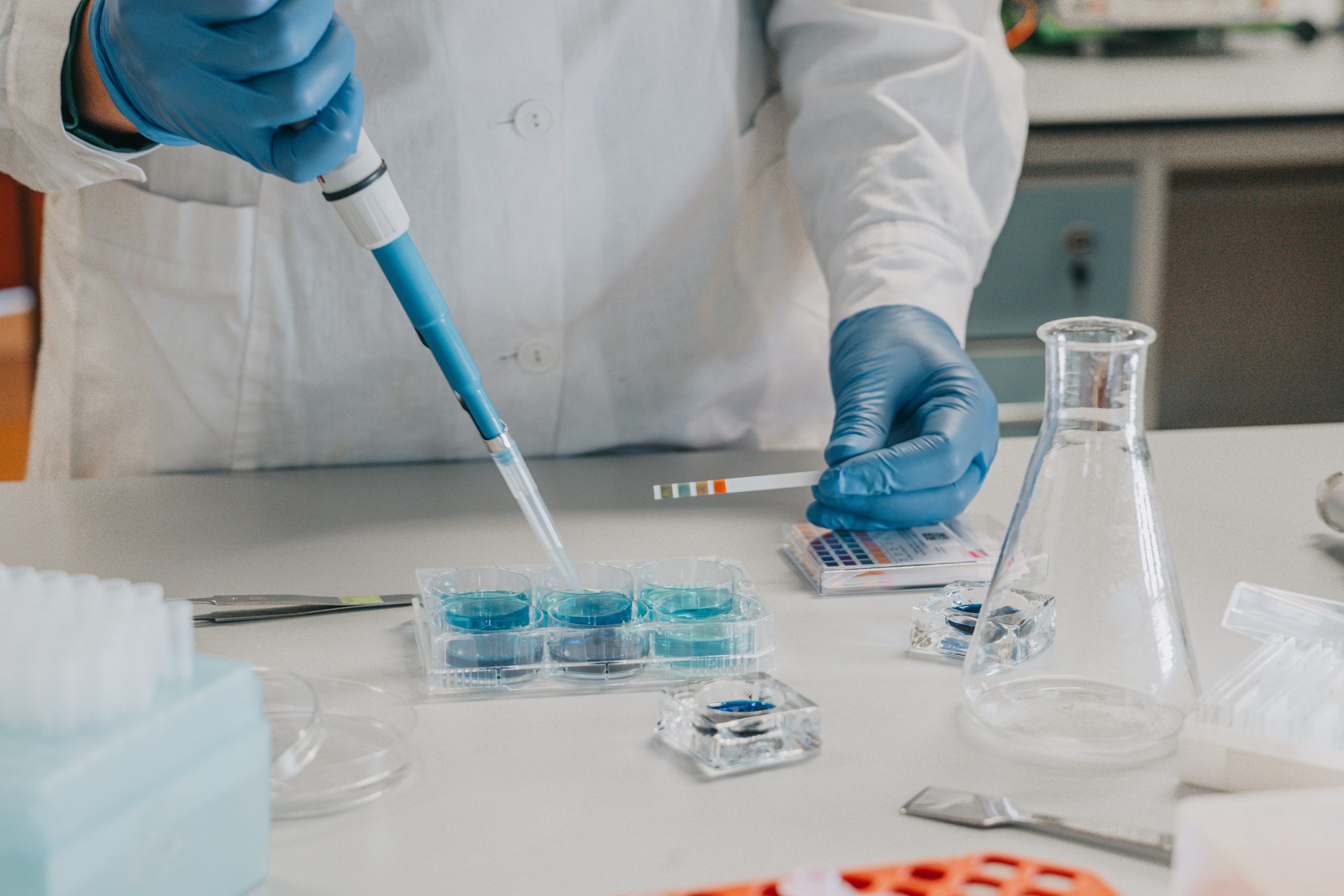 Laboratorium badawcze. Osoba w fartuchu laboratoryjnym pipetuje.